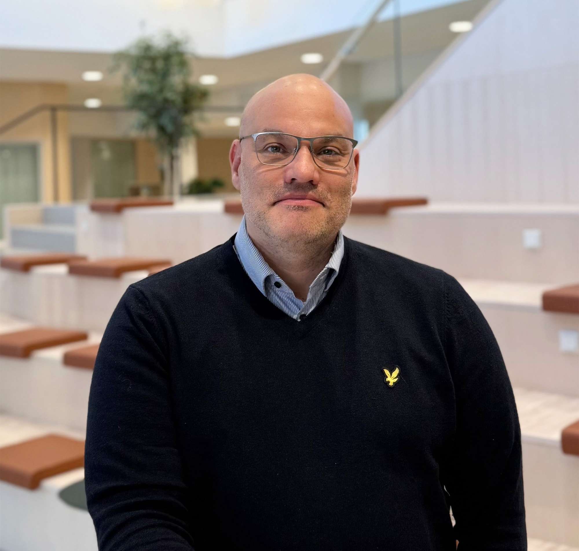 Man står och lutar sig mot ett ståbord, tittar in i kameran och ler