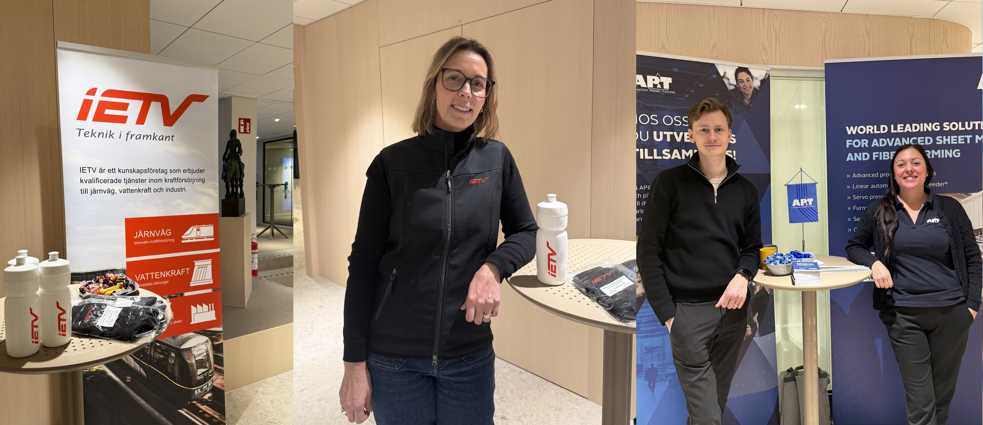 En rollup vid ett ståbord med några vattenflaskor på, en kvinna står och hänger vid ett ståbord, tittar in i kameran och ler, en kvinna och en man står framför en rollup, tittar in i kameran och ler