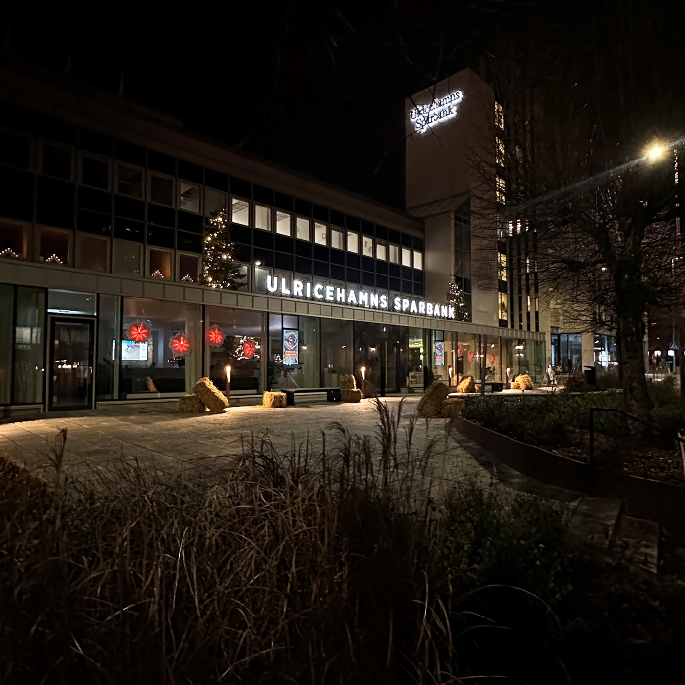 En bankentre i mörker, ljusskylt Ulricehamns Sparbank, jultstjärnor i fönstren