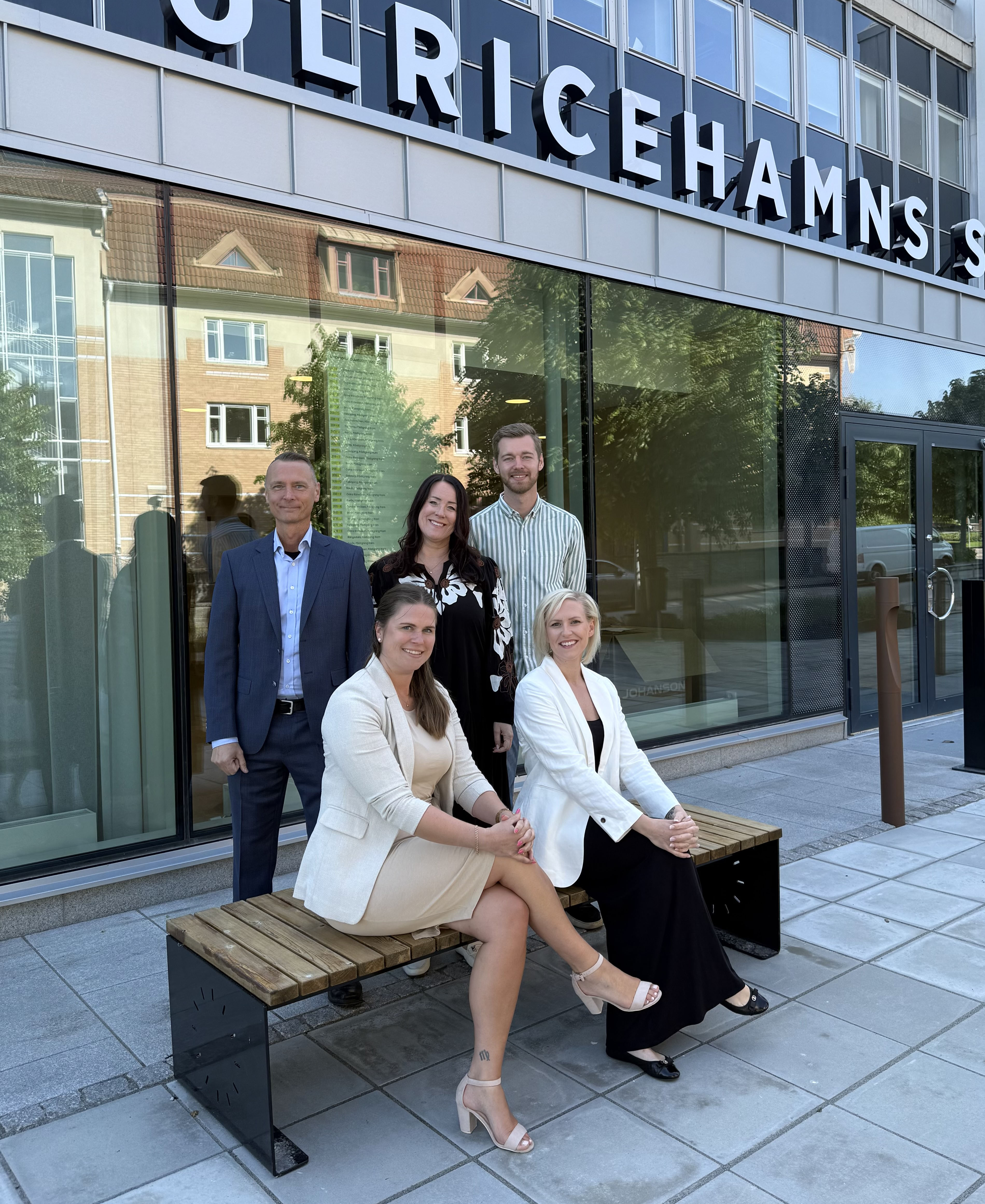 Fem personer står och sitter på en bänk utanför ett bankkontor