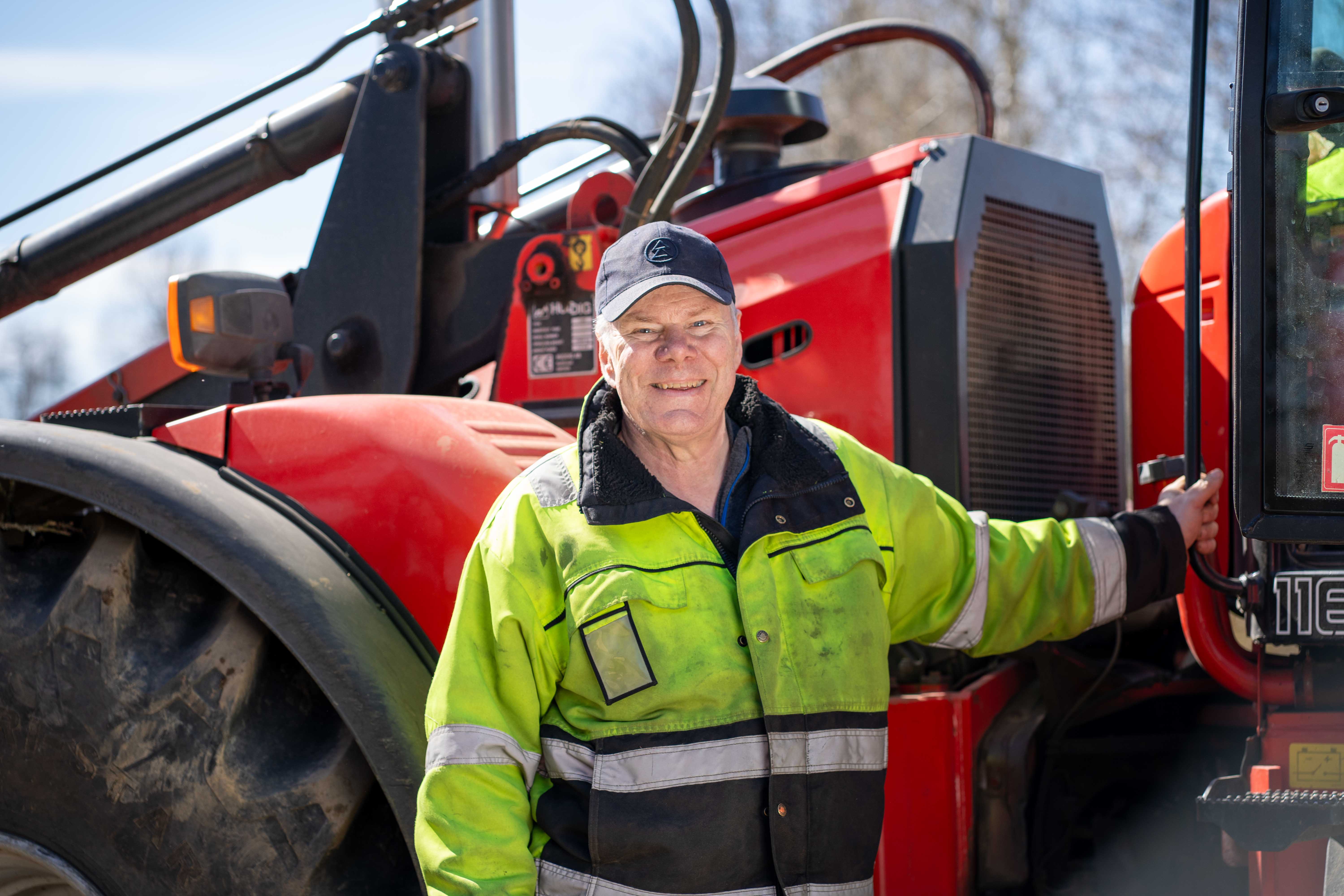 Man håller i ett handtag på en röd traktor, tittar in i kameran och ler