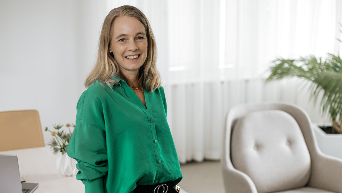 Leende kvinna i en grön blus tittar i kameran